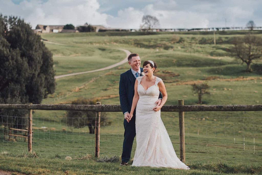 Bride and Groom laugh in front of rolling hills on their wedding day at Kingscote Barn