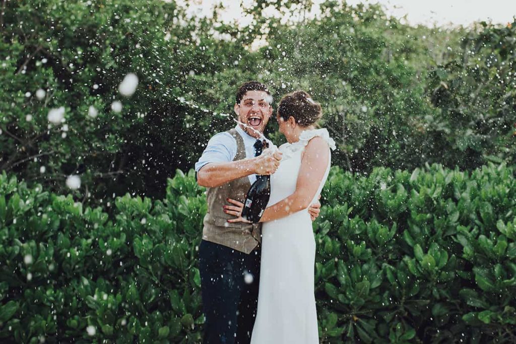 Groom sprays champagne bottle over bride and groom whilst laughing