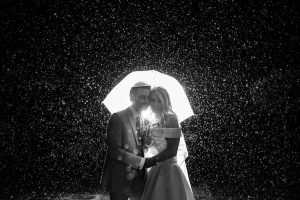 married couple standing under umbrella in the rain at night