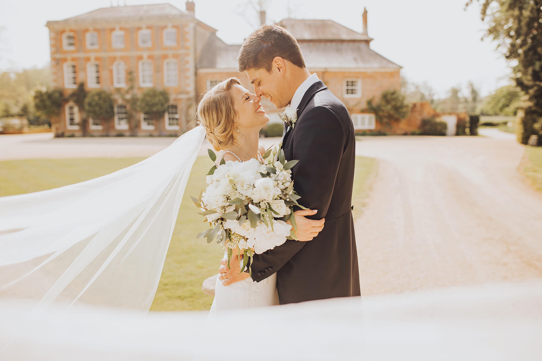 April wedding at Syrencot House. cewlywed Couple stand infront of the georgian wedding venue with the bride's veil blowing in the wind.