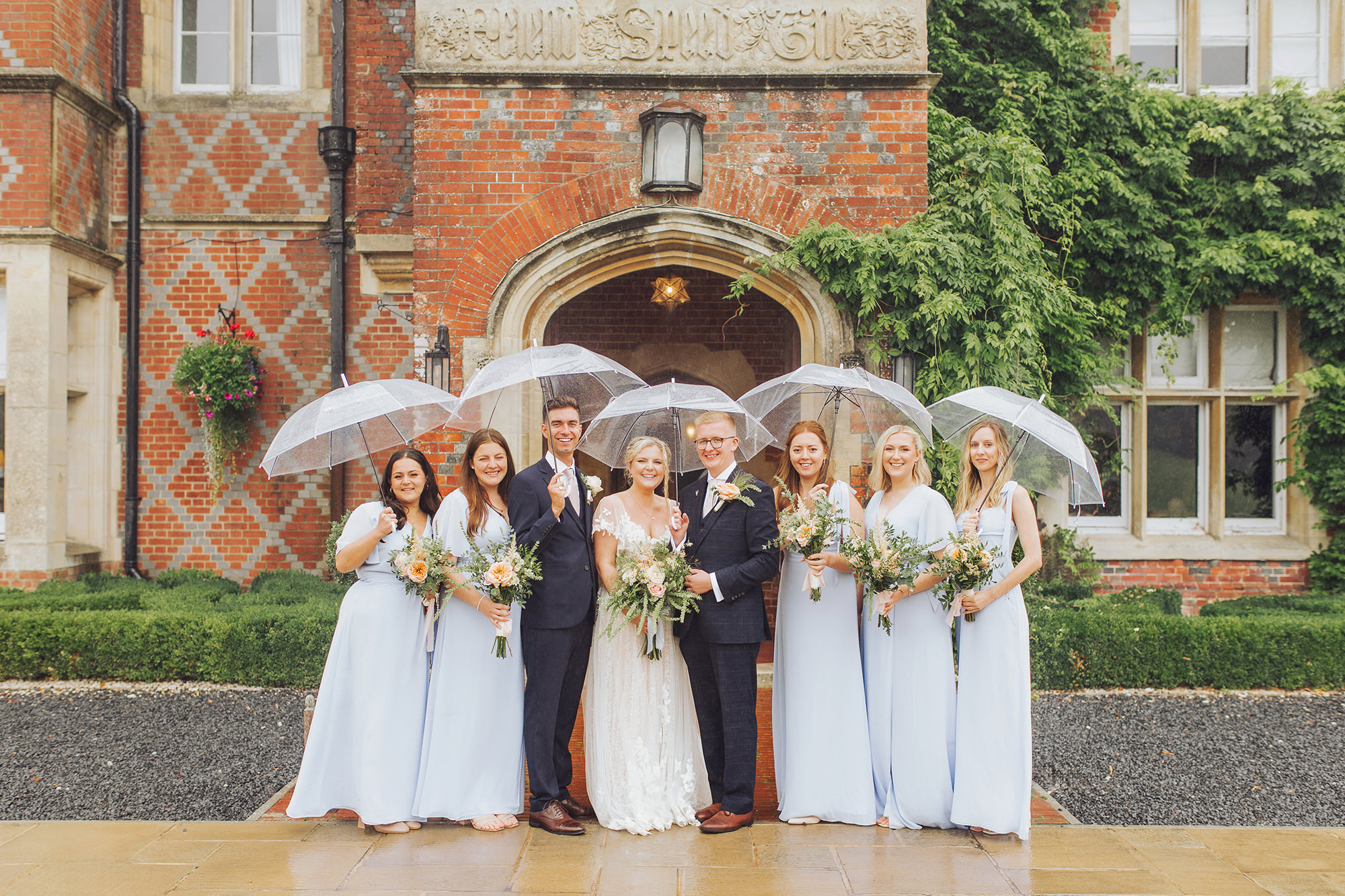 a rainy wedding party group photo at burley manor under clear umbrellas
